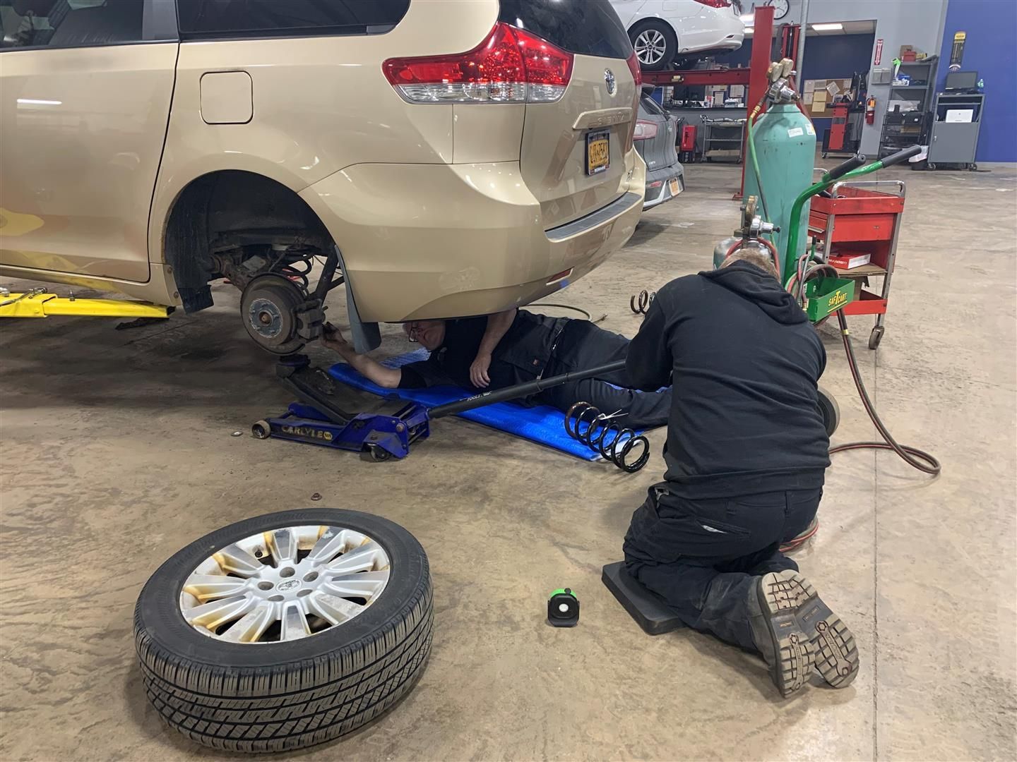 A man is working under a car in a garage. | Lou's Car Care Center Inc.