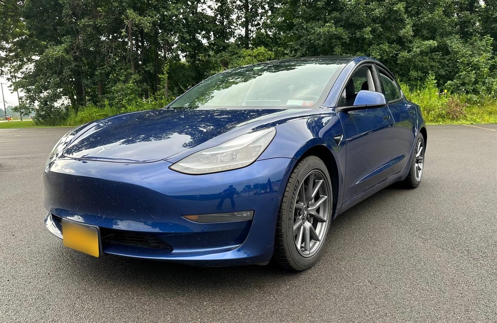 A blue tesla model 3 is parked on the side of the road. | Lou's Car Care Center, Inc.