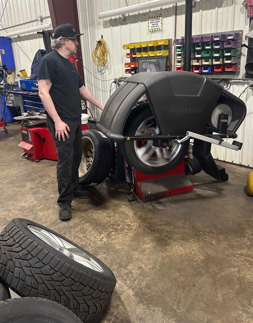 A man is standing next to a tire balancing machine in a garage.  | Lou's Car Care Center, Inc.