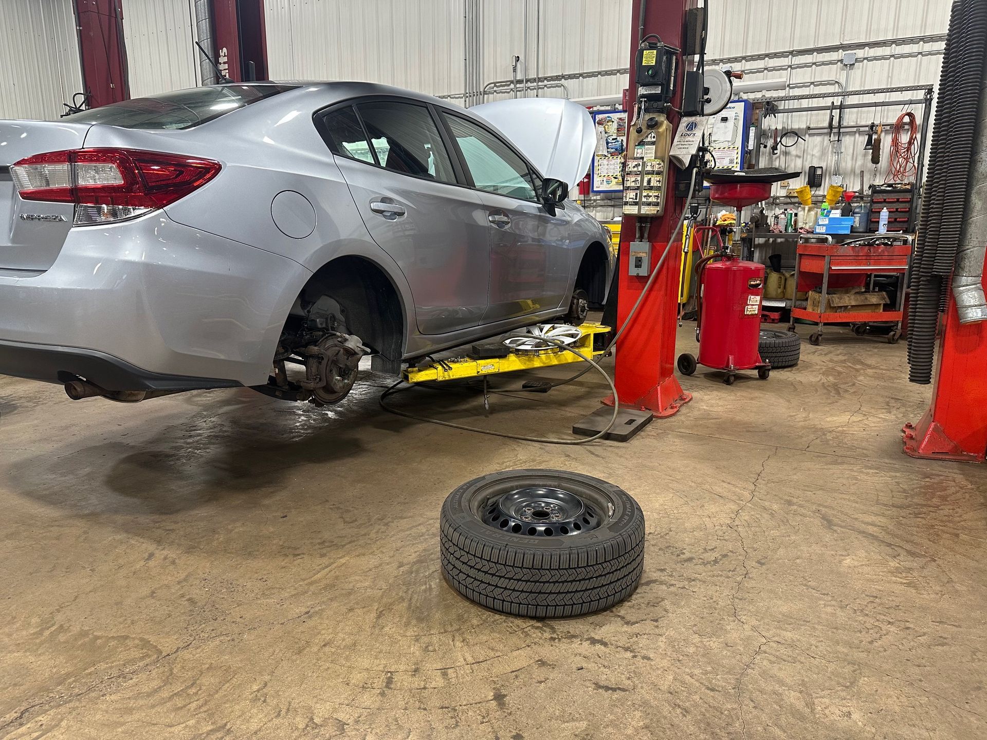 A car is sitting on a lift in a garage next to a tire.  | Lou's Car Care Center, Inc.