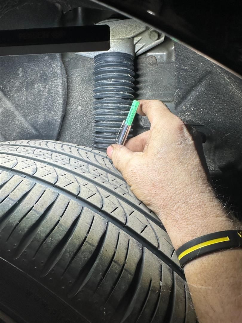 A person is holding a green marker over a tire.  | Lou's Car Care Center, Inc.