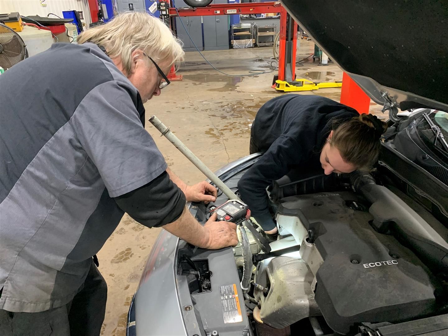 A man and a woman are working on the engine of a car. | Lou's Car Care Center Inc.