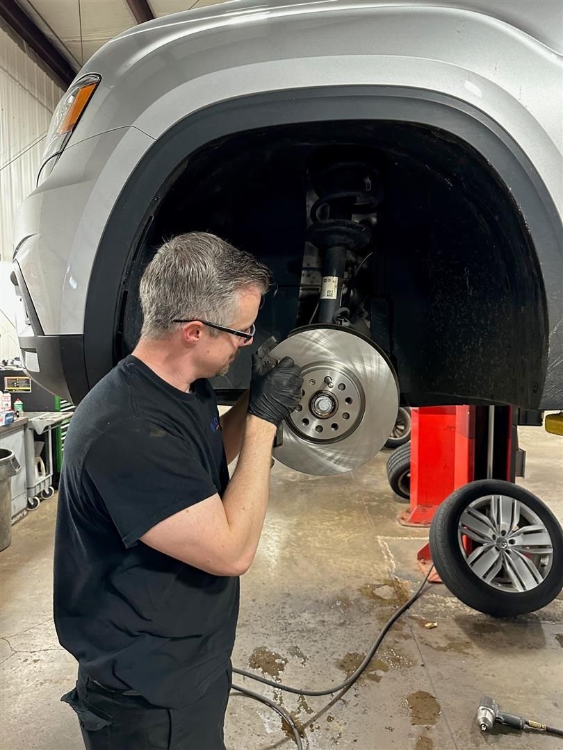 A man is working on the brake rotor of a car in a garage. | Lou's Car Care Center, Inc.