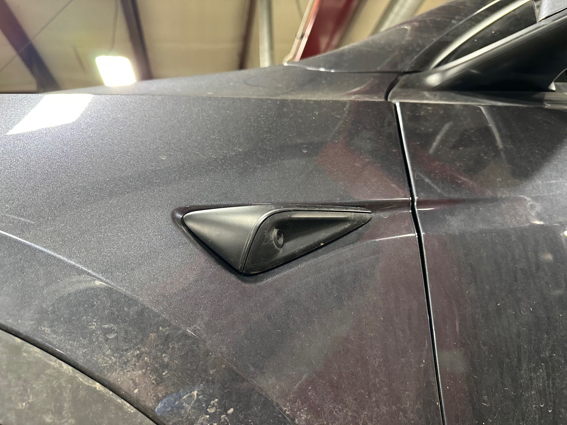 Vehicle ADAS camera in dark grey Tesla vehicle fender.