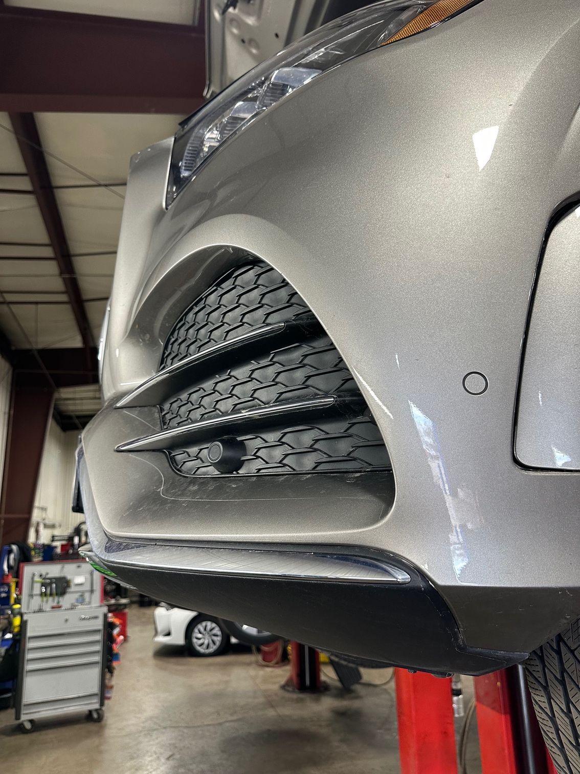 Vehicle ADAS sensors on front bumper of grey vehicle.