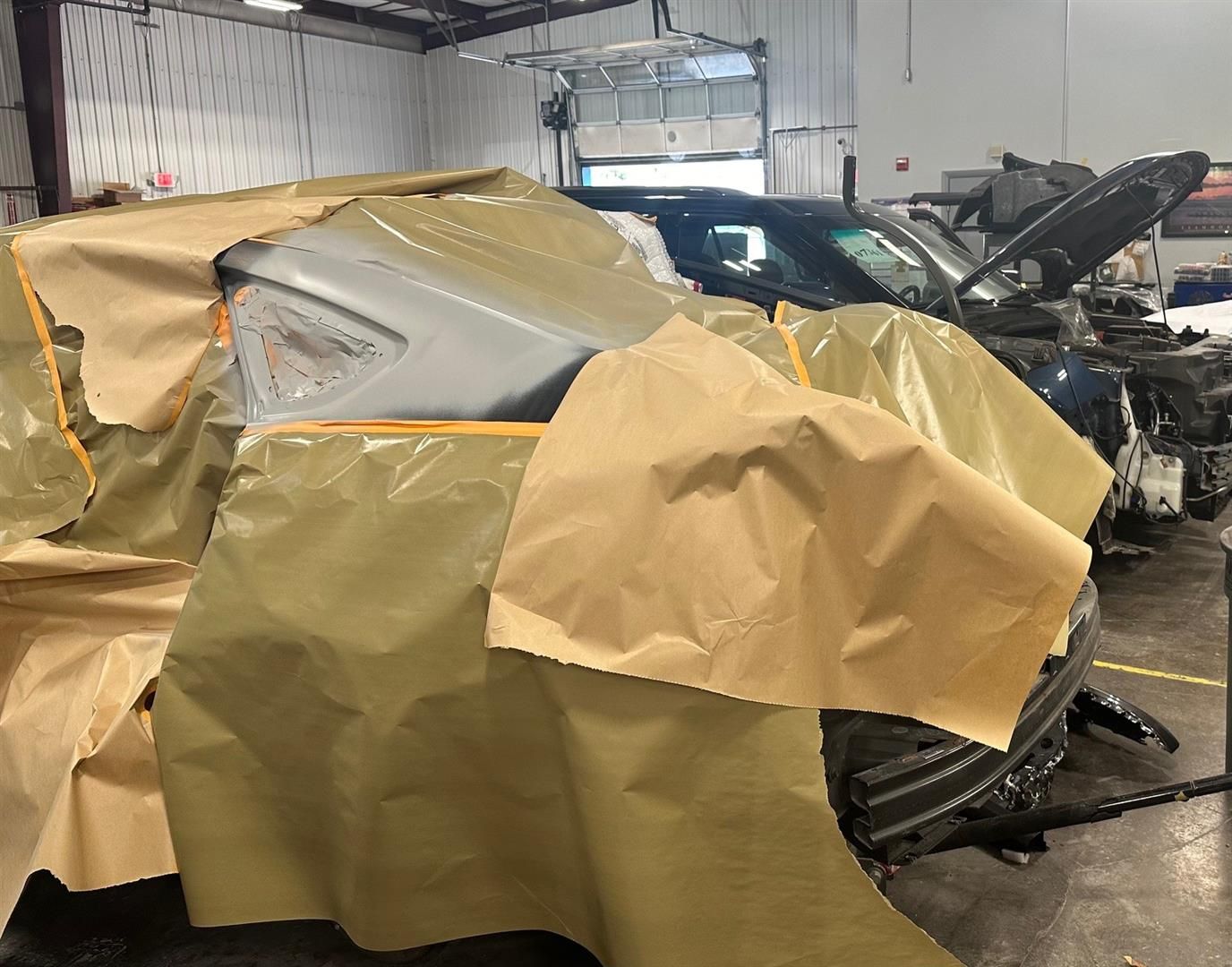 A car is covered in plastic wrap in a garage.  | Lou's Car Care Center, Inc.