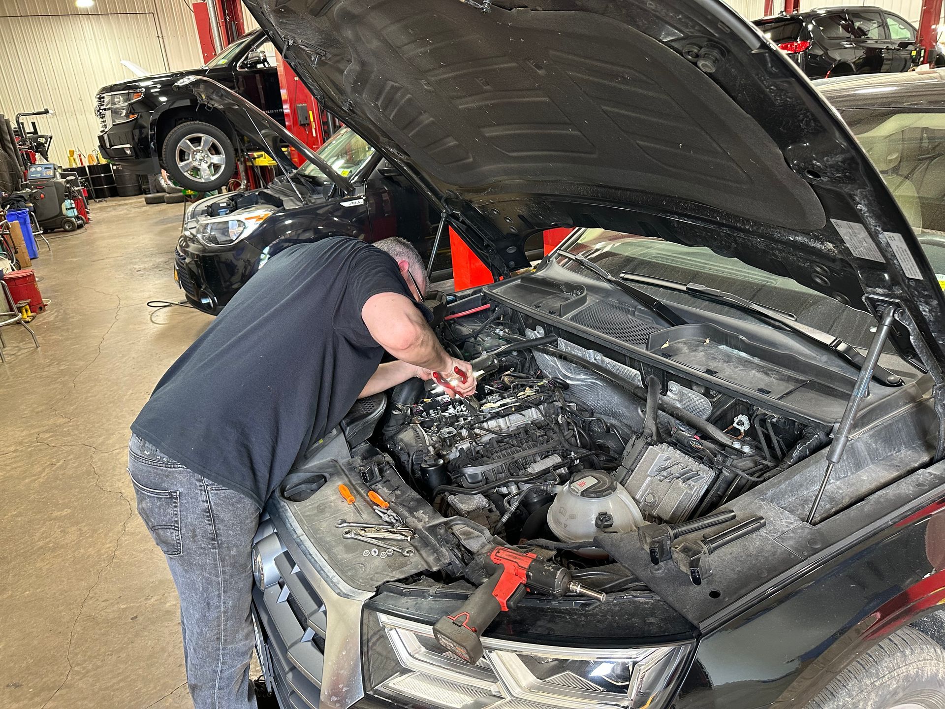 A man is working under the hood of a car in a garage.  | Lou's Car Care Center, Inc.