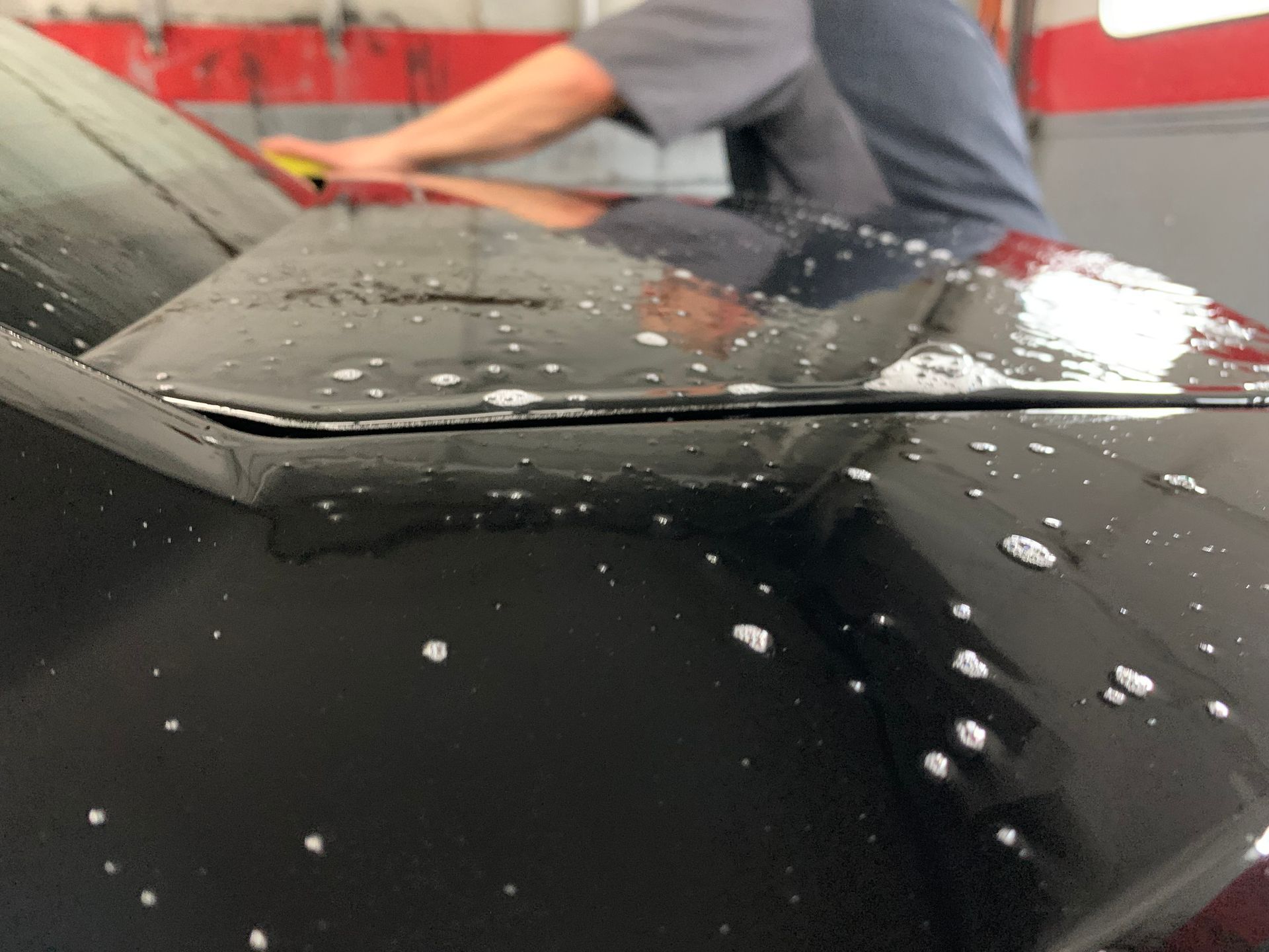 A man is cleaning the hood of a black car | Lou's Car Care Center