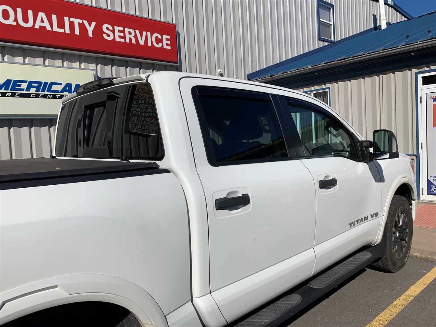 A white truck is parked in front of a quality service building. | Lou's Car Care Center, Inc.