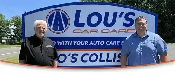 Father and son standing in front of sign for shop | Lou's Car Care Center