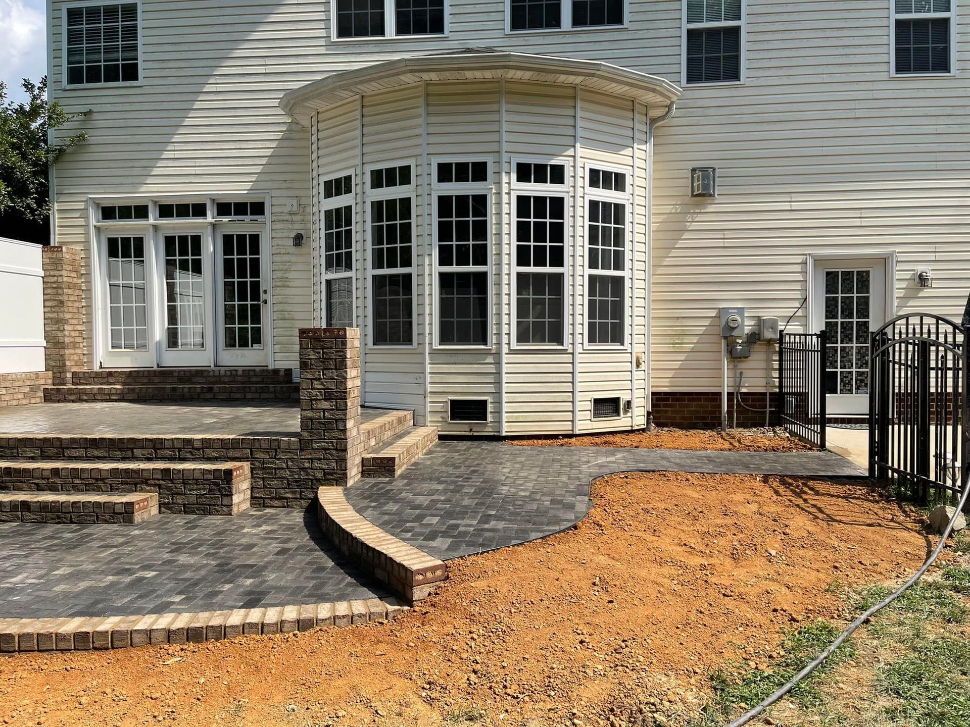 Backyard with brick patio, curved walkway, and sunroom attached to a two-story beige house.