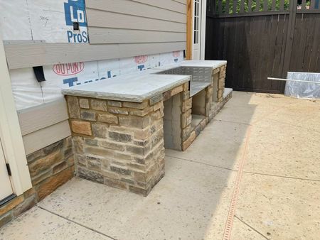 Stone benches with concrete tops against a building's exterior. A door is on the left.
