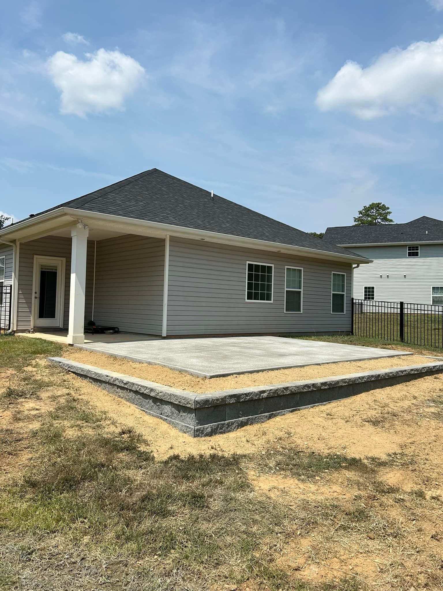 Backyard patio under construction with gray siding house and retaining wall.