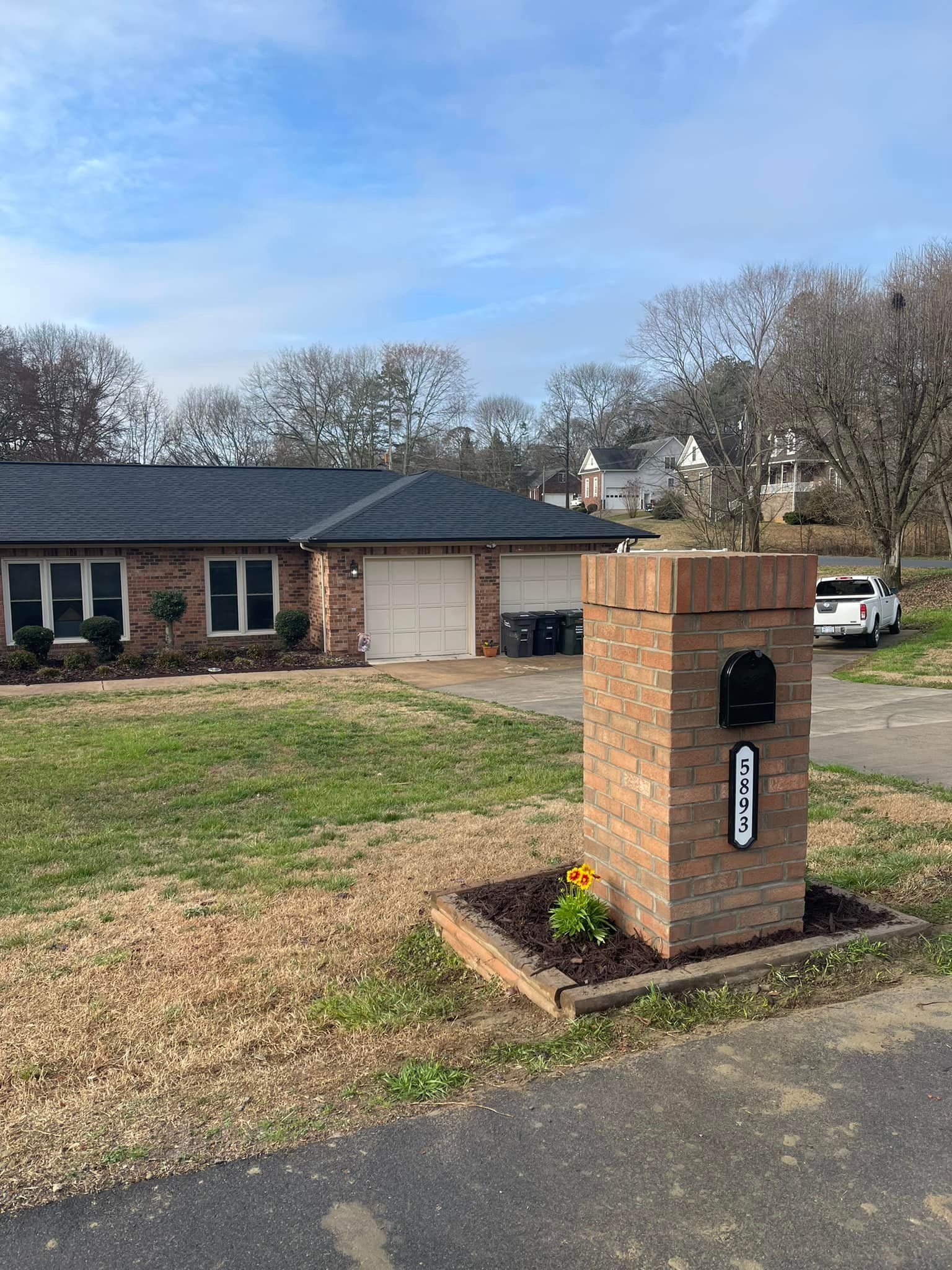 Brick mailbox with address, in front of a brick house with garages, on a sunny day.