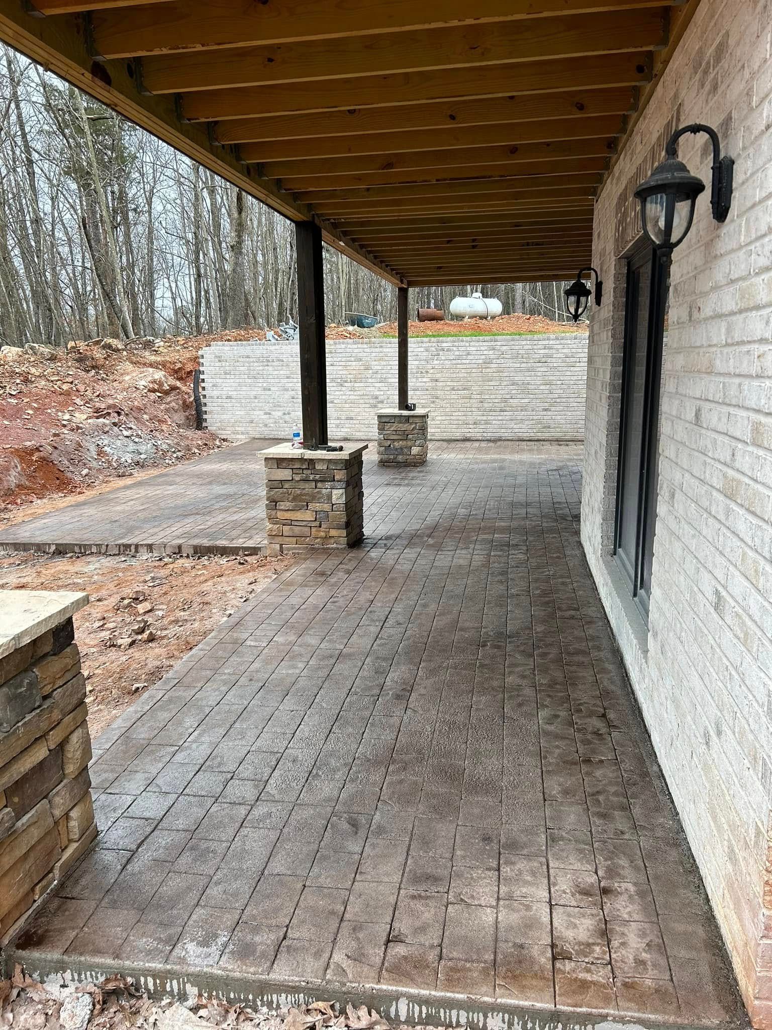 Covered porch with stamped concrete floor and brick wall. Wooden support posts with stone accents.
