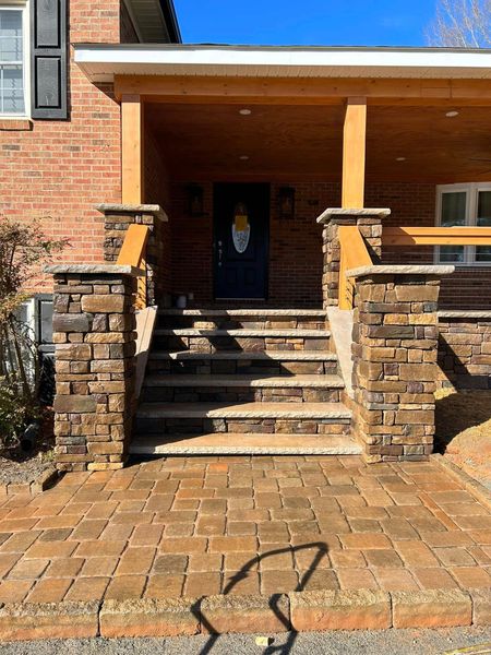 Stone steps and walkway lead to a house with a covered porch and dark front door.