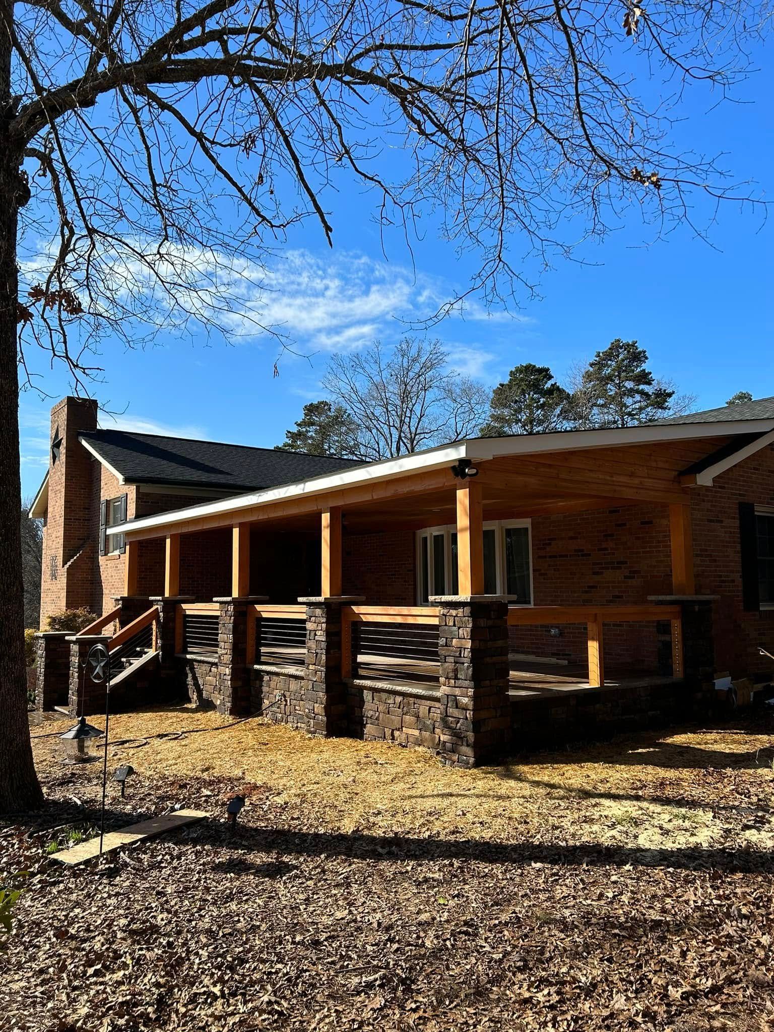House with brick facade and covered porch, blue sky, tree in the foreground.