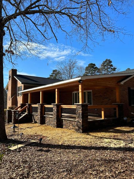 House with brick facade and covered porch, blue sky, tree in the foreground.
