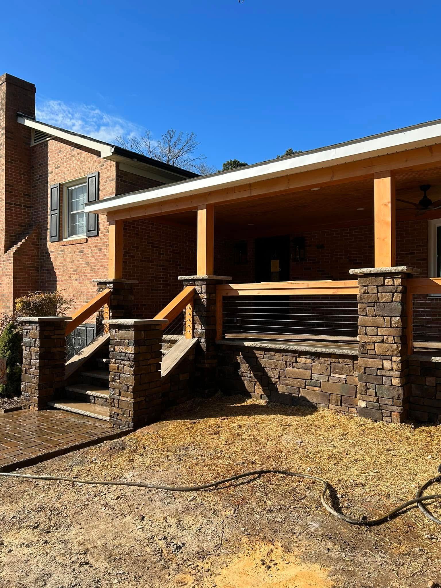 Brick house with covered porch, stone pillars, wooden railing, and blue sky.