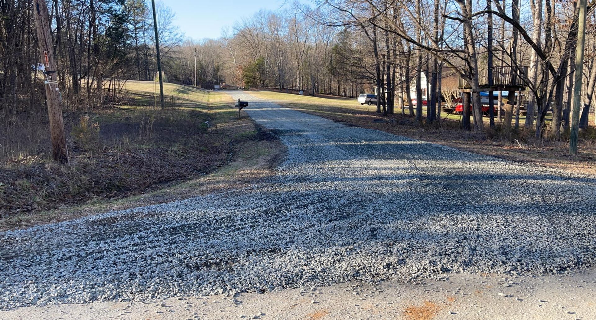 Gravel road leading into a wooded area with bare trees and a blue sky.