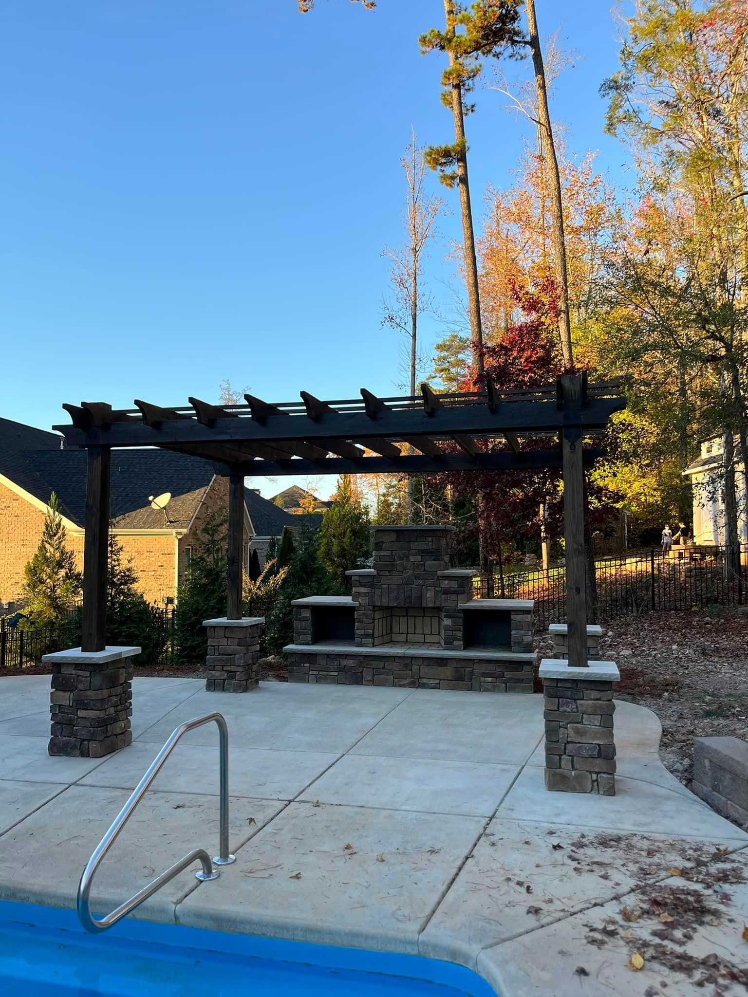 Pergola with fireplace by a pool on a sunny day.