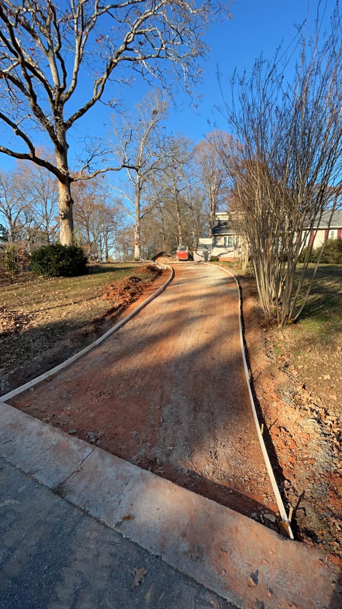 Gravel pathway bordered by concrete curbing, leading toward houses under a blue sky.