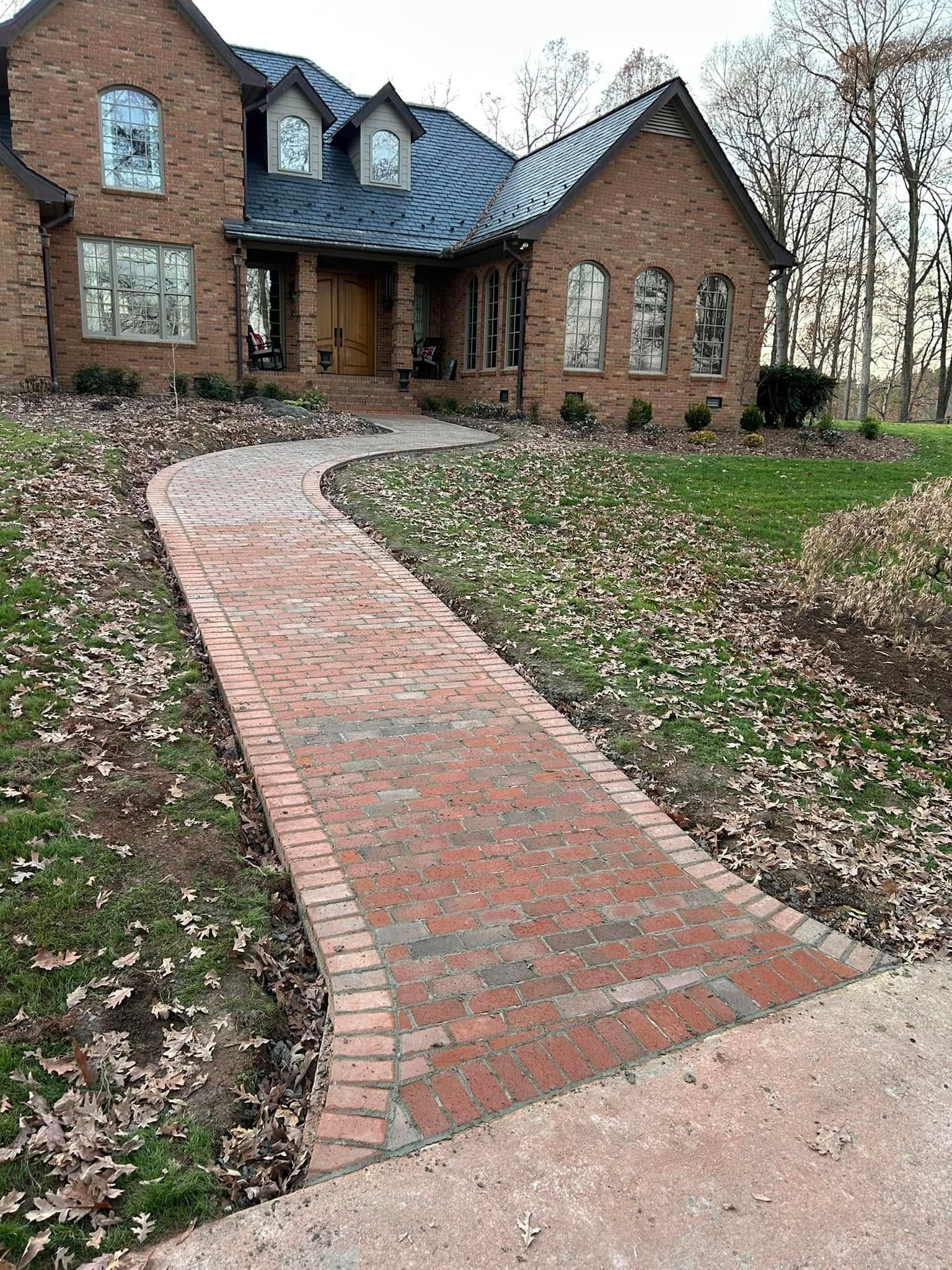 Brick pathway leading to a brick home with arched windows and a dark roof.