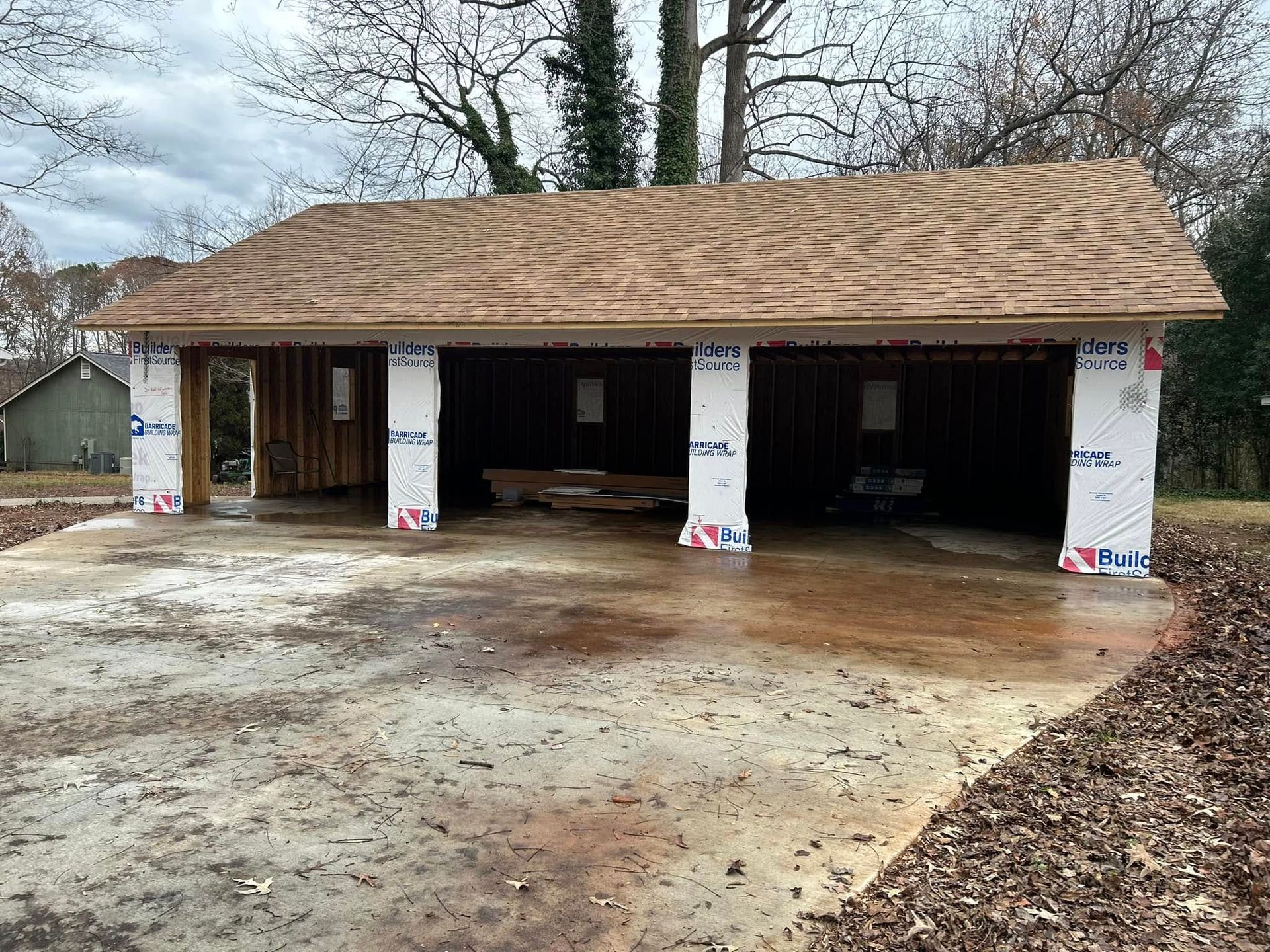 A partially constructed carport with a brown roof and concrete foundation.  Columns are wrapped in white protective covering.