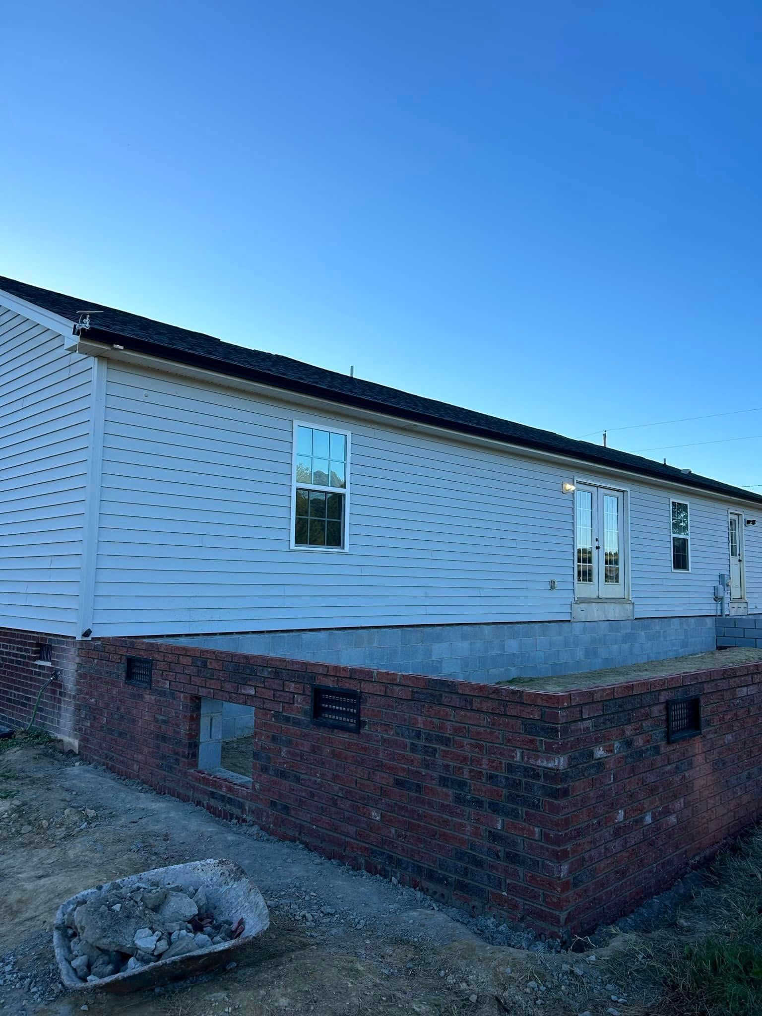 Side view of a house under construction with brick foundation and light blue siding against a clear sky.