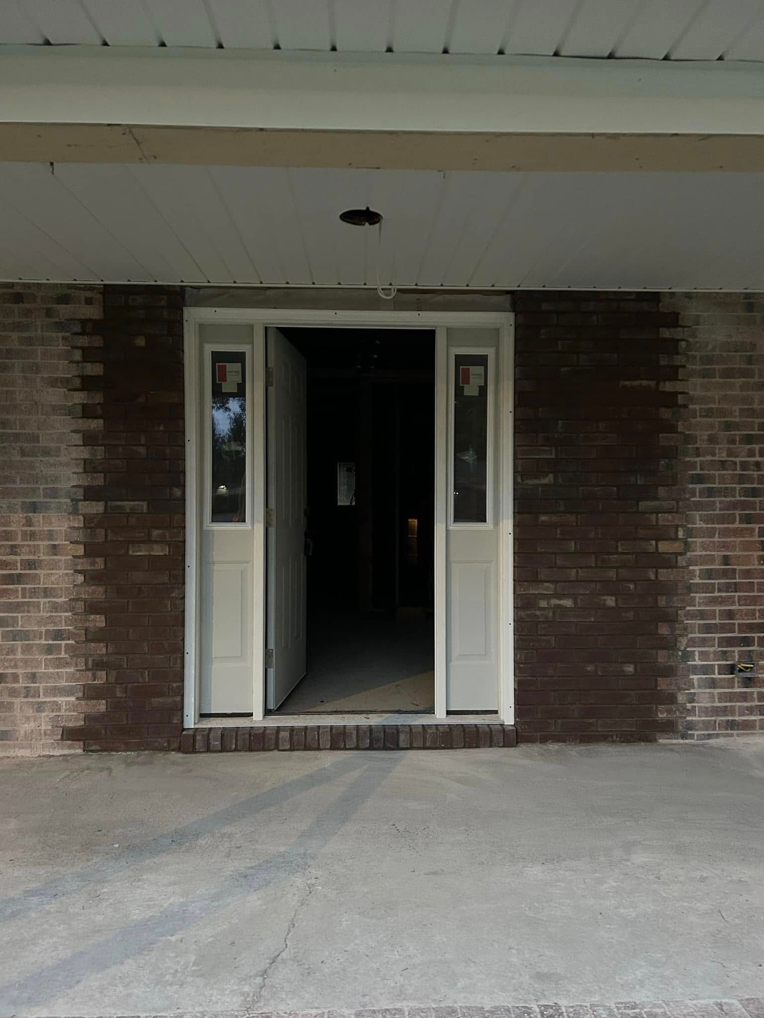 Exterior of a brick building entrance with a white door, two side panels, and a concrete porch.