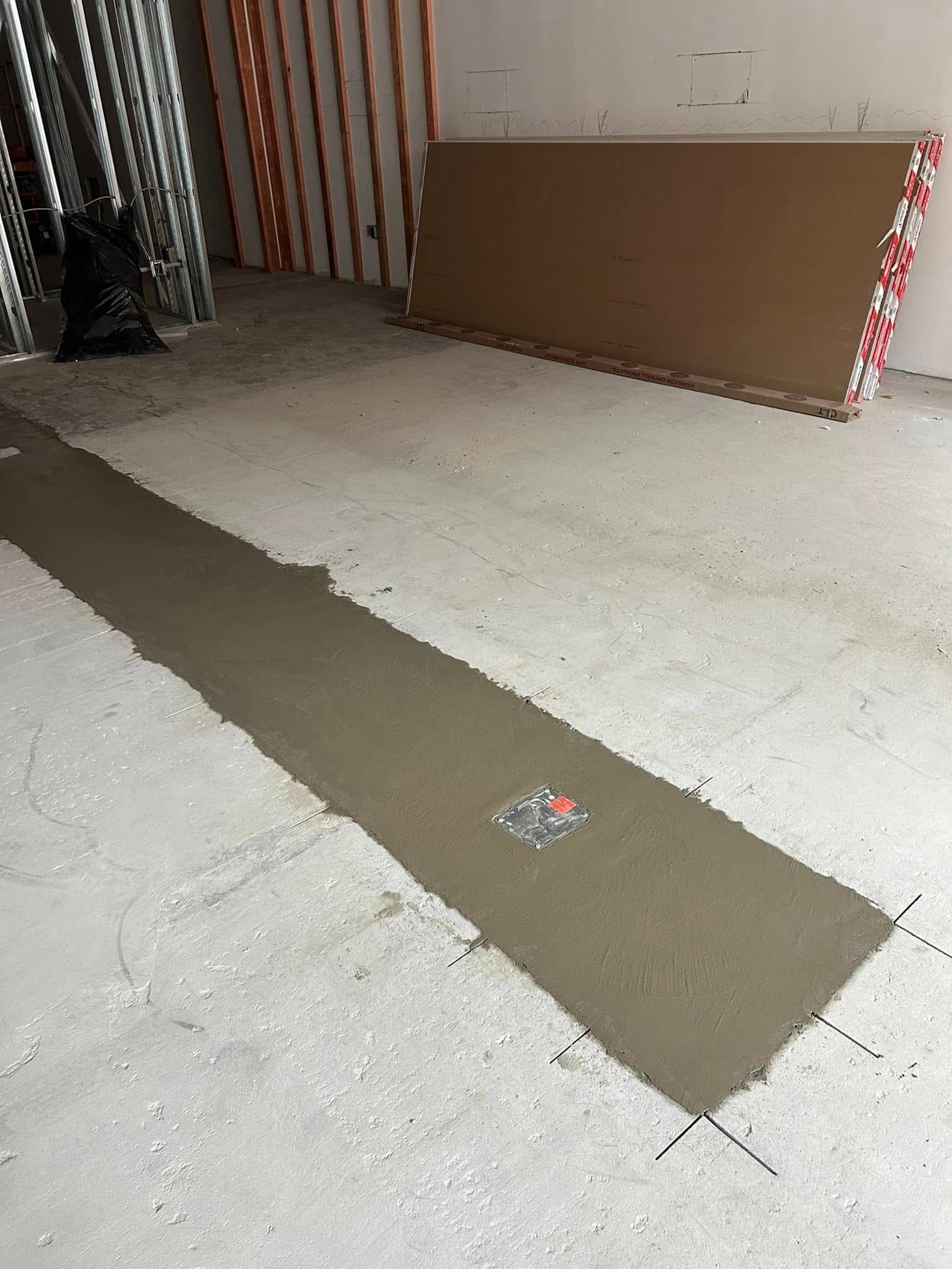 Concrete work in progress on a floor. A long rectangular section is filled with fresh concrete.