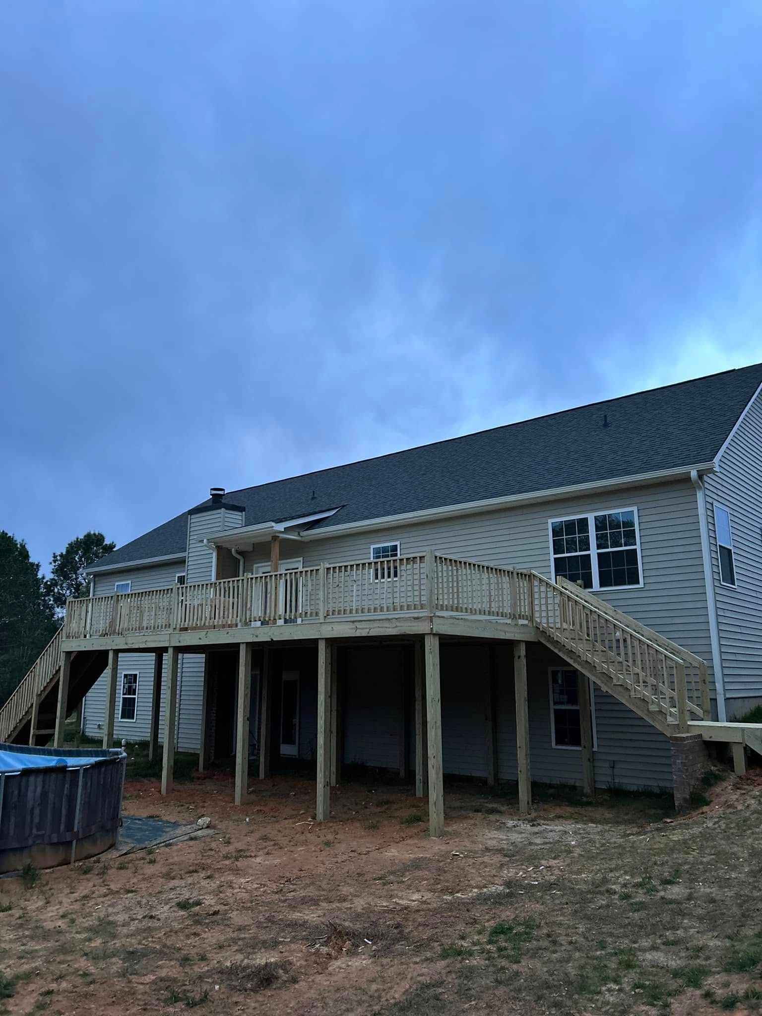 Newly constructed wooden deck attached to a two-story house with stairs, set in a yard under a cloudy sky.