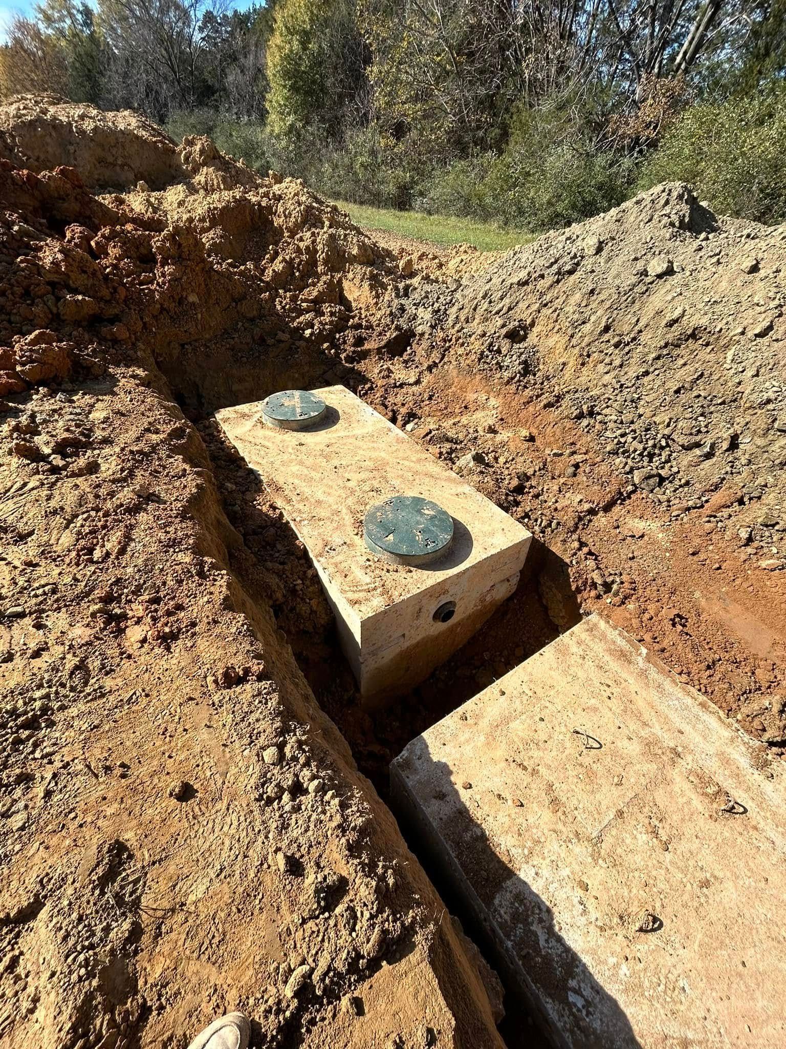 Concrete blocks with lids in a trench dug in dirt, outdoors.
