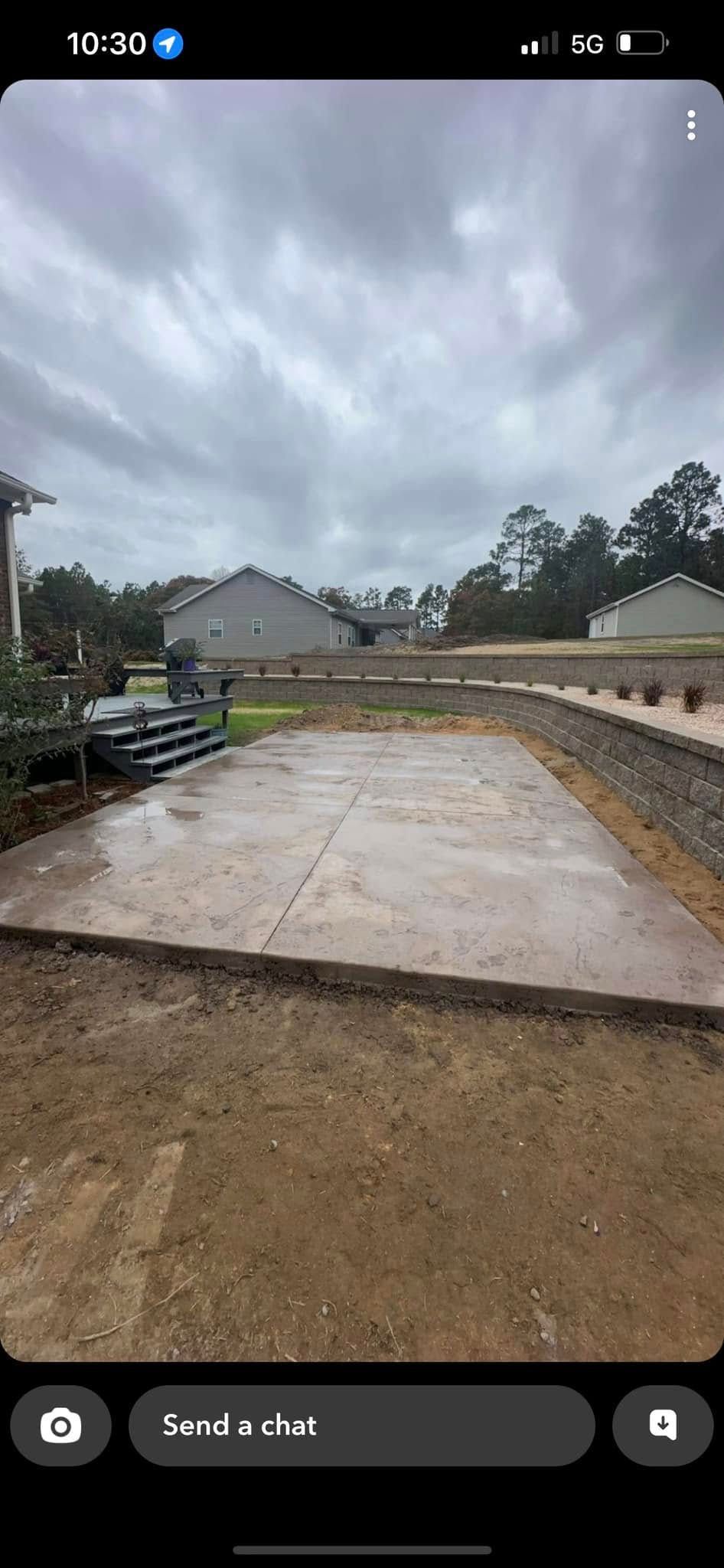 Outdoor view of a concrete slab surrounded by dirt and landscaping under a cloudy sky.