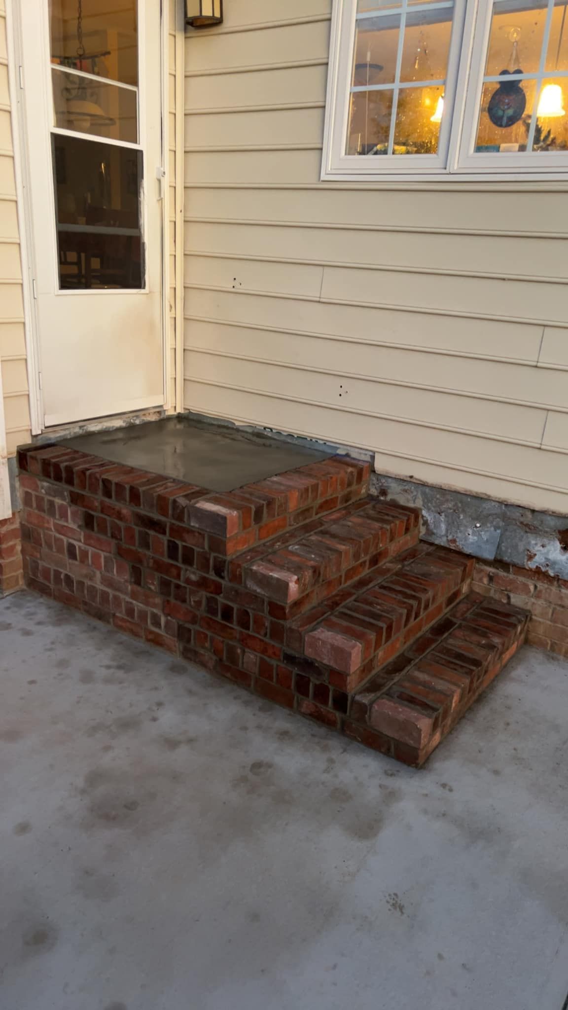 Brick steps leading up to a white door, with a concrete landing. A cream-colored wall is behind the steps.