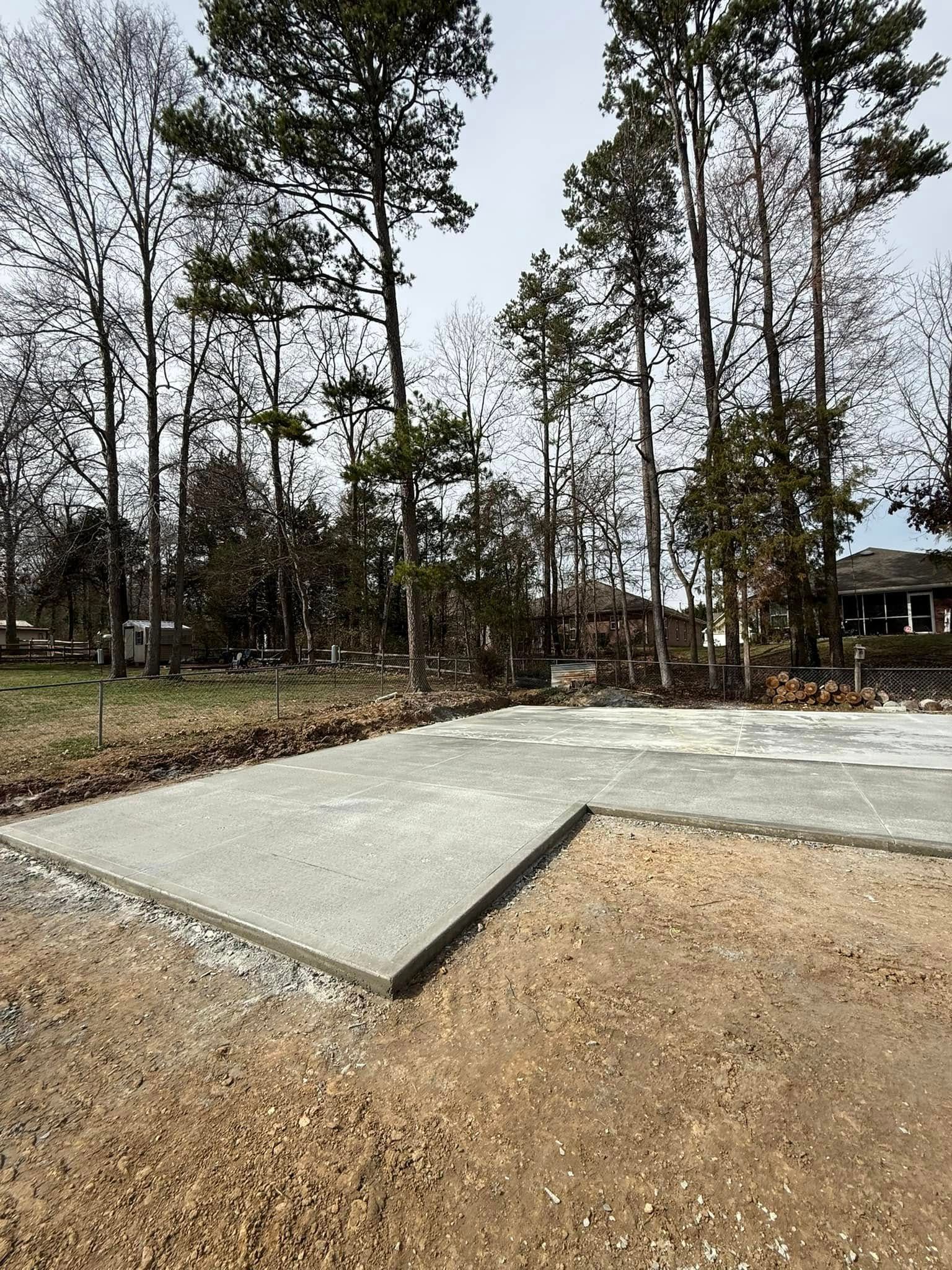 Concrete slab in a sandy lot, framed by brown soil and trees against a cloudy sky.
