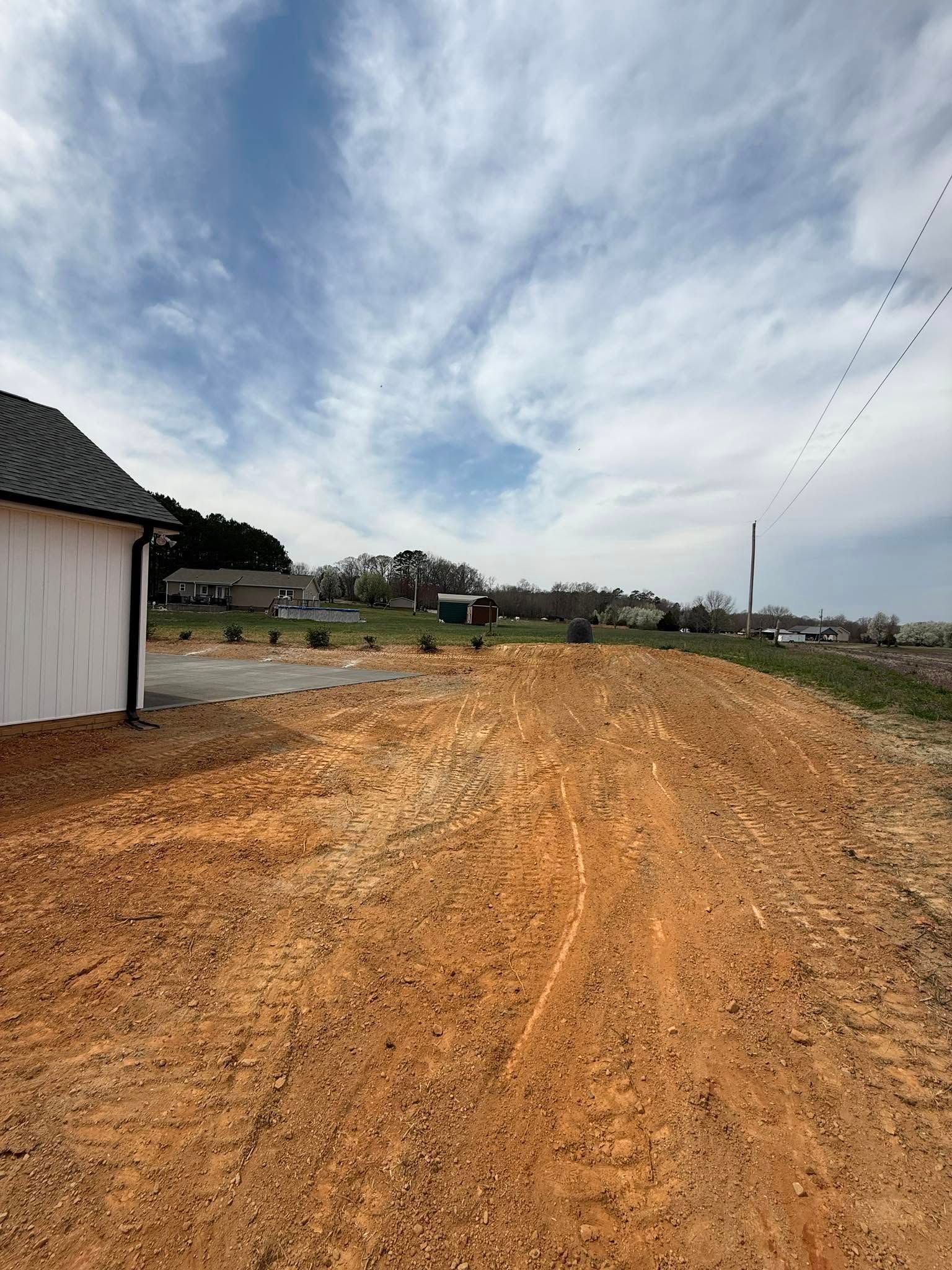 Dirt path with a white building and a line of birds against a cloudy sky.