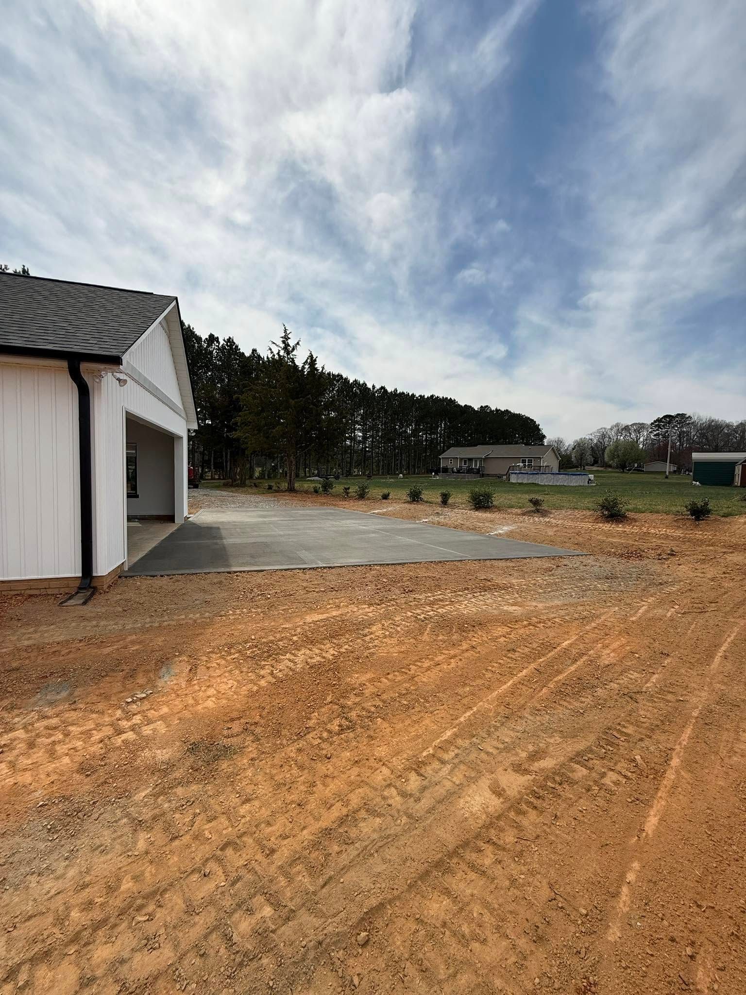 Garage next to a paved area and dirt, blue sky, trees in the background.