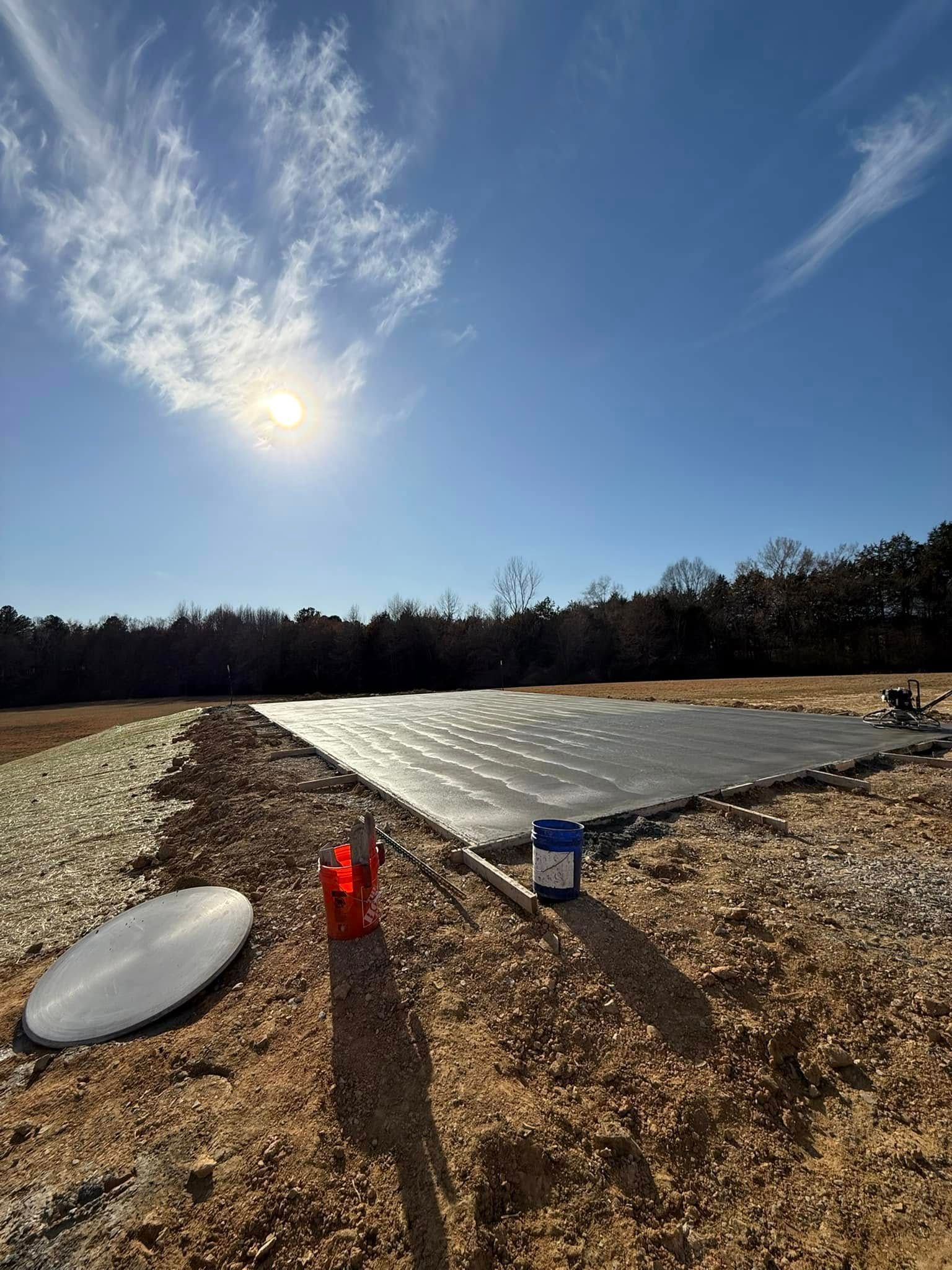 Sunlit outdoor scene of black mats laid on a dirt field; bucket and other supplies nearby.