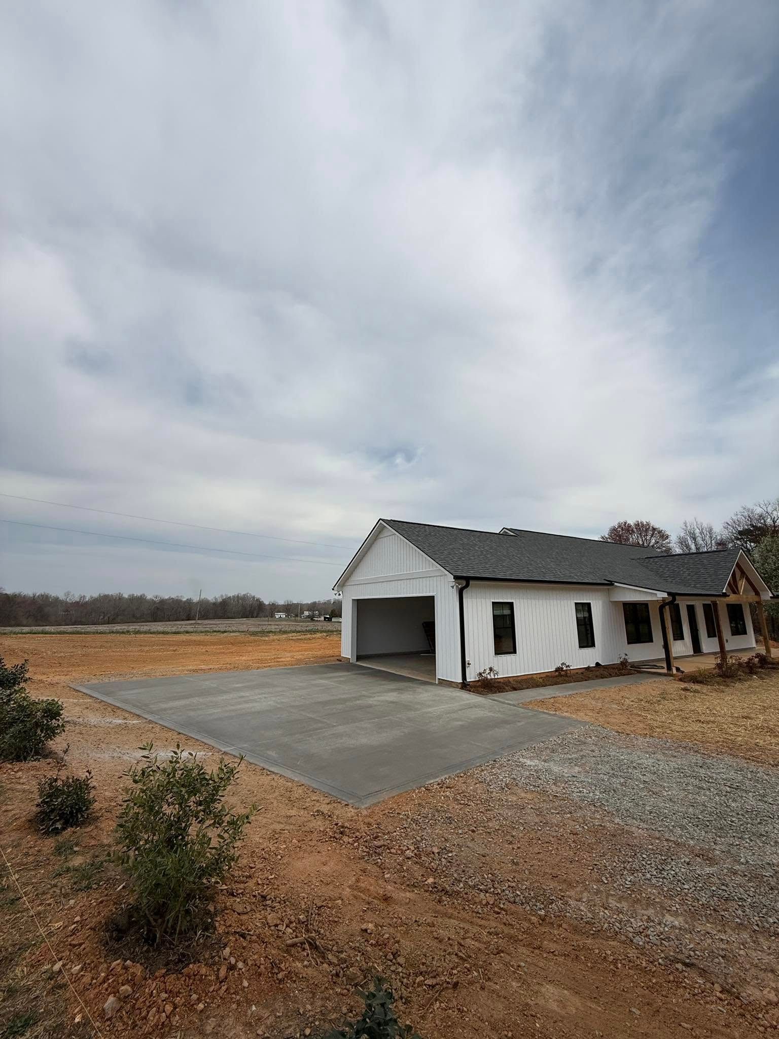 White house under construction, with open garage, on a dirt and gravel lot, against a cloudy sky.