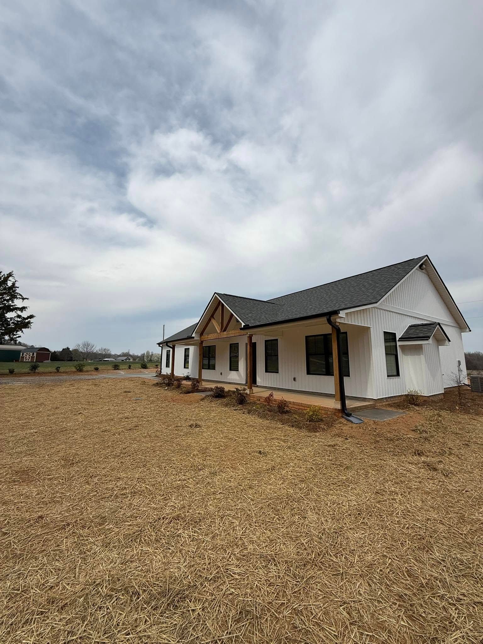 New home construction, white siding, dark roof, wood beams, gravel yard, cloudy sky.