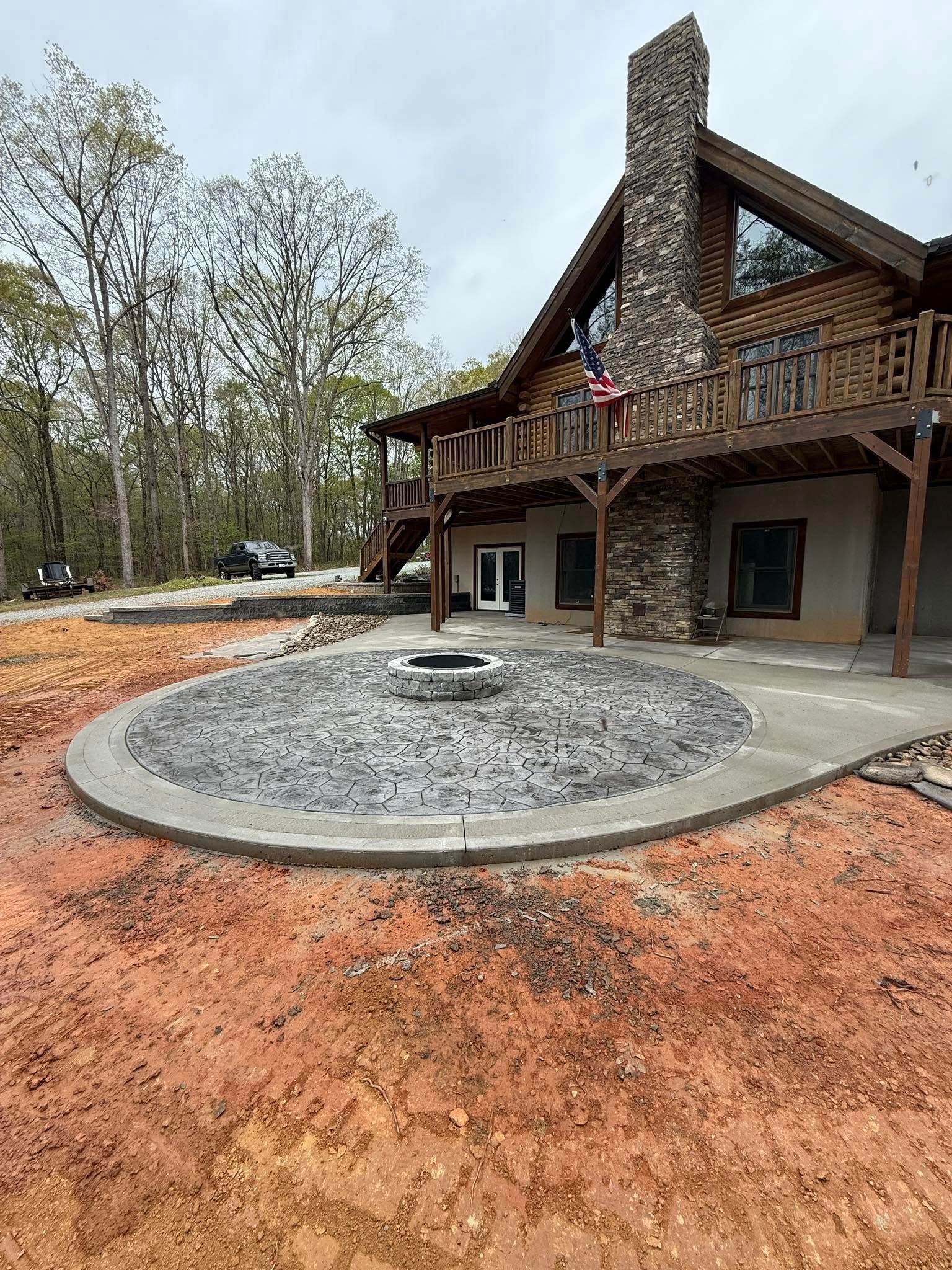 Cabin with a stone chimney, wraparound porch, and a circular fire pit with gray rocks.
