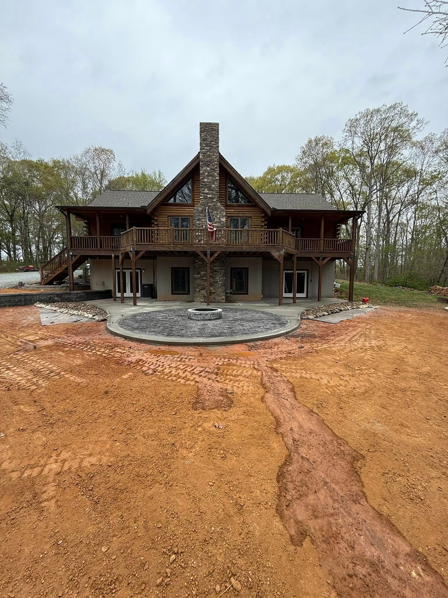 Rustic cabin with stone chimney, wooden balconies, set on a red dirt clearing. Overcast sky.
