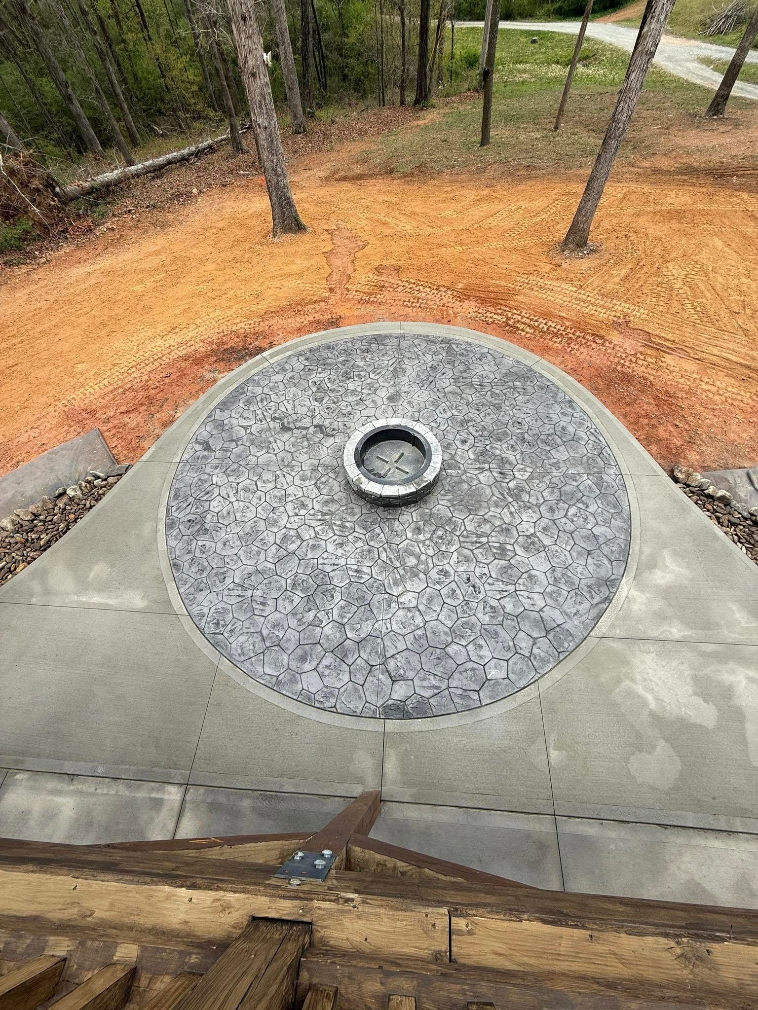 Overhead view of a circular stone fire pit with a metal ring, surrounded by tan mulch and trees.