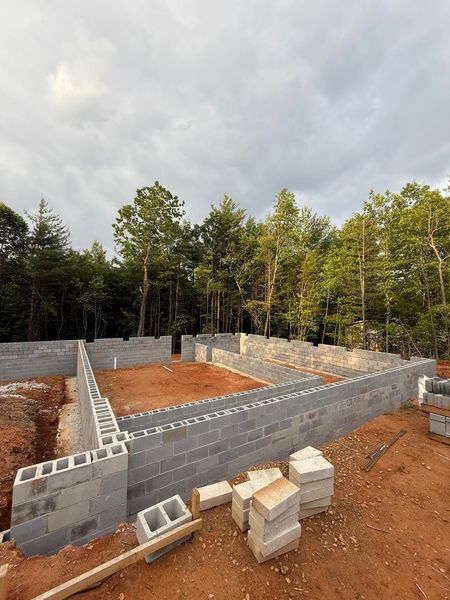 Foundation of a building constructed with concrete blocks, with a wooded backdrop under a cloudy sky.