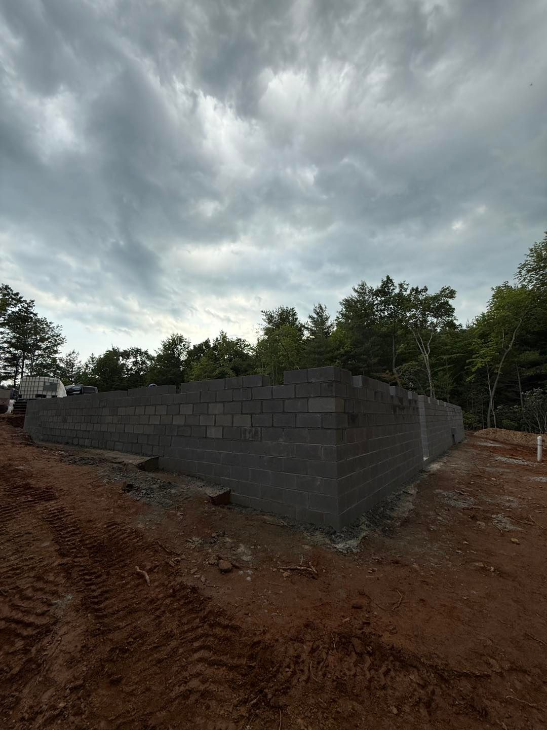 Gray cinder block foundation walls under construction, dirt lot, overcast sky, trees in the background.