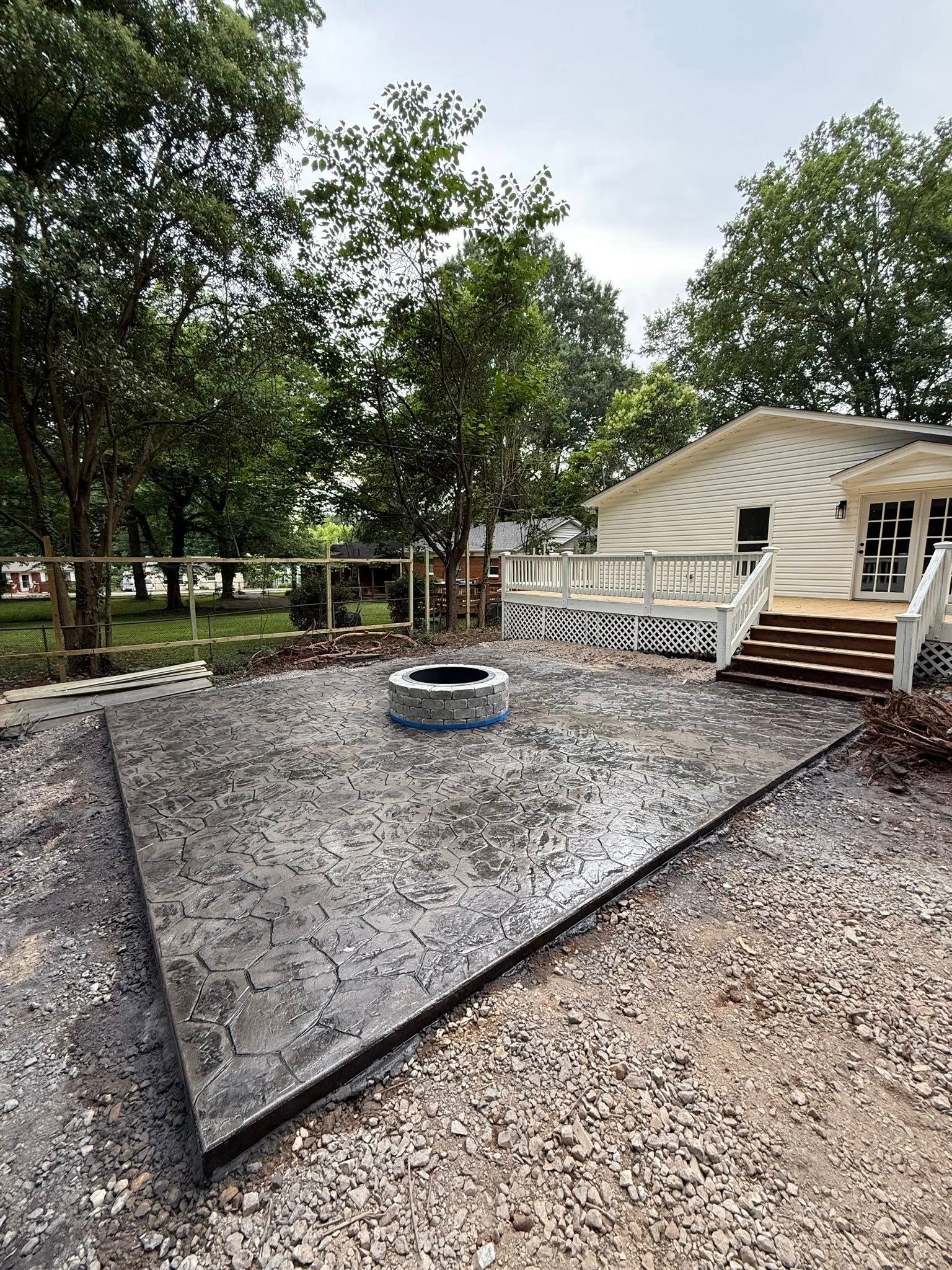 Exterior view of a house with a concrete patio, fire pit, and wooden stairs, surrounded by trees.