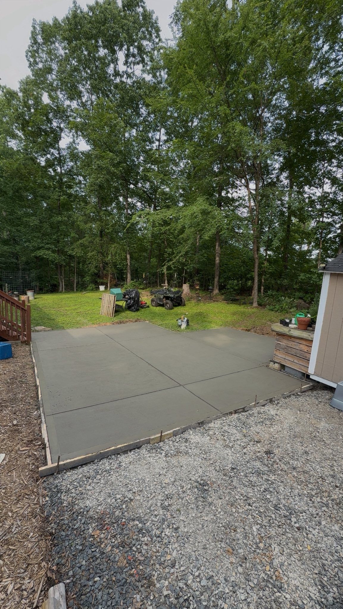 Newly poured concrete patio, surrounded by gravel and trees in a wooded area.
