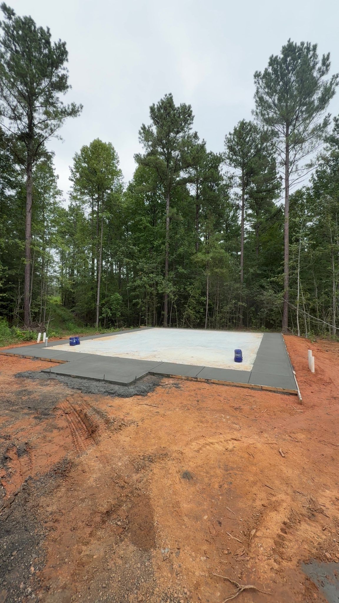 Newly cleared land with a concrete pad surrounded by dirt, trees in background.