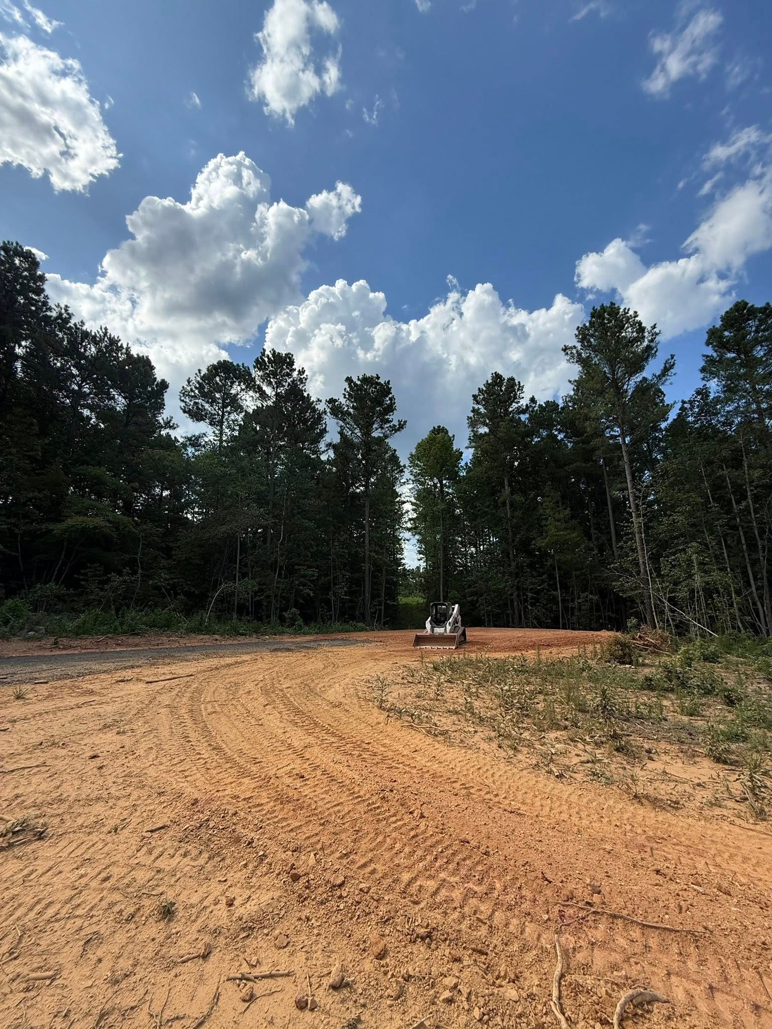 Dirt road leading to a treeline under a blue sky with white clouds.